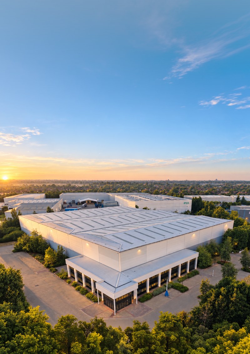 Milton Keynes 111 from the air at sunset: a large refurbished white warehouse with a two-storey glazed office front, surrounded by mature trees