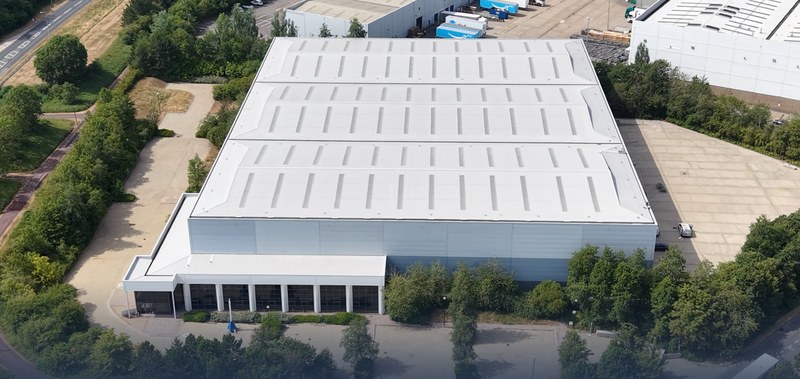 Milton Keynes 111 from above: the white-clad warehouse and its glazed two-storey office front, the gated yard to one side and trees all round